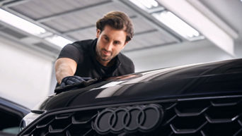 Mann mit Handschuhen poliert die schwarze Motorhaube eines Audi in heller Werkstatt.