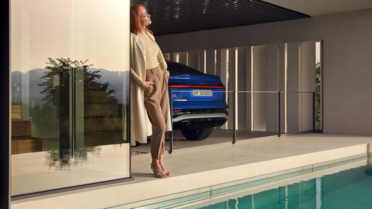 Eine Frau lehnt an einer Tür, im Hintergrund steht ein blauer Audi