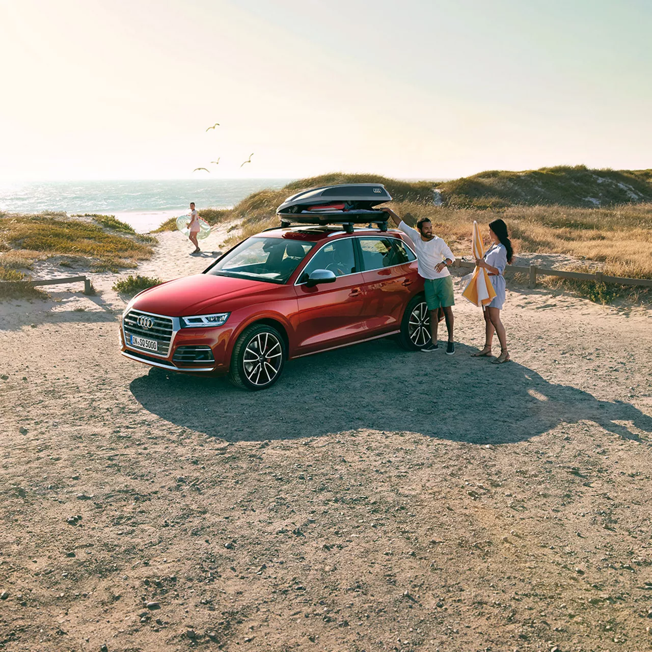 Ein roter Audi steht am Strand, drumherum ist eine Familie