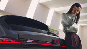 Junge Frau lehnt am Heck ihres Audi A6 e-tron