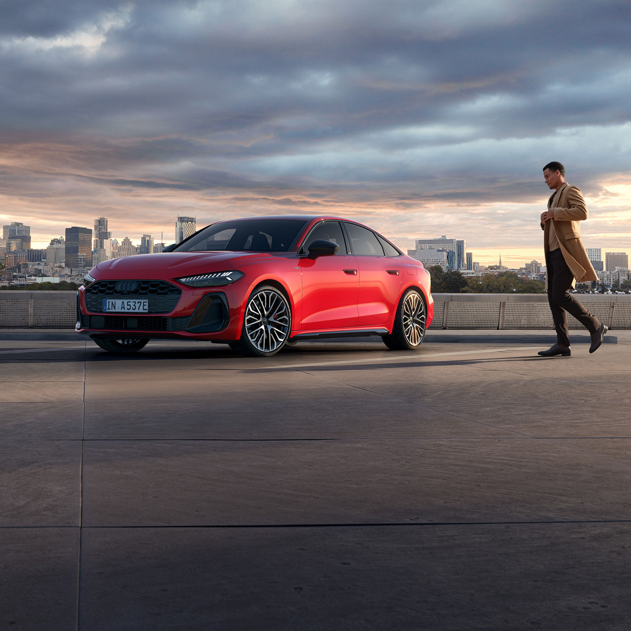 Roter Audi steht vor Skyline bei Sonnenuntergang, Mann im Mantel nähert sich dem Auto von rechts.