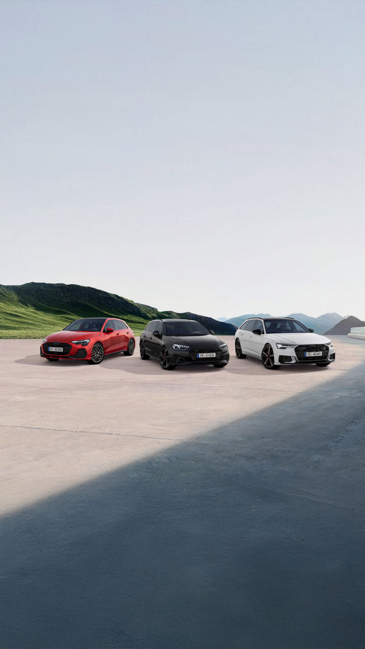 Gruppenbild mit einem roten A3 Sportback, einem schwarzen A4 Avant und einem weißen A6 Avant auf einem Parkplatz vor alpiner Kulisse.