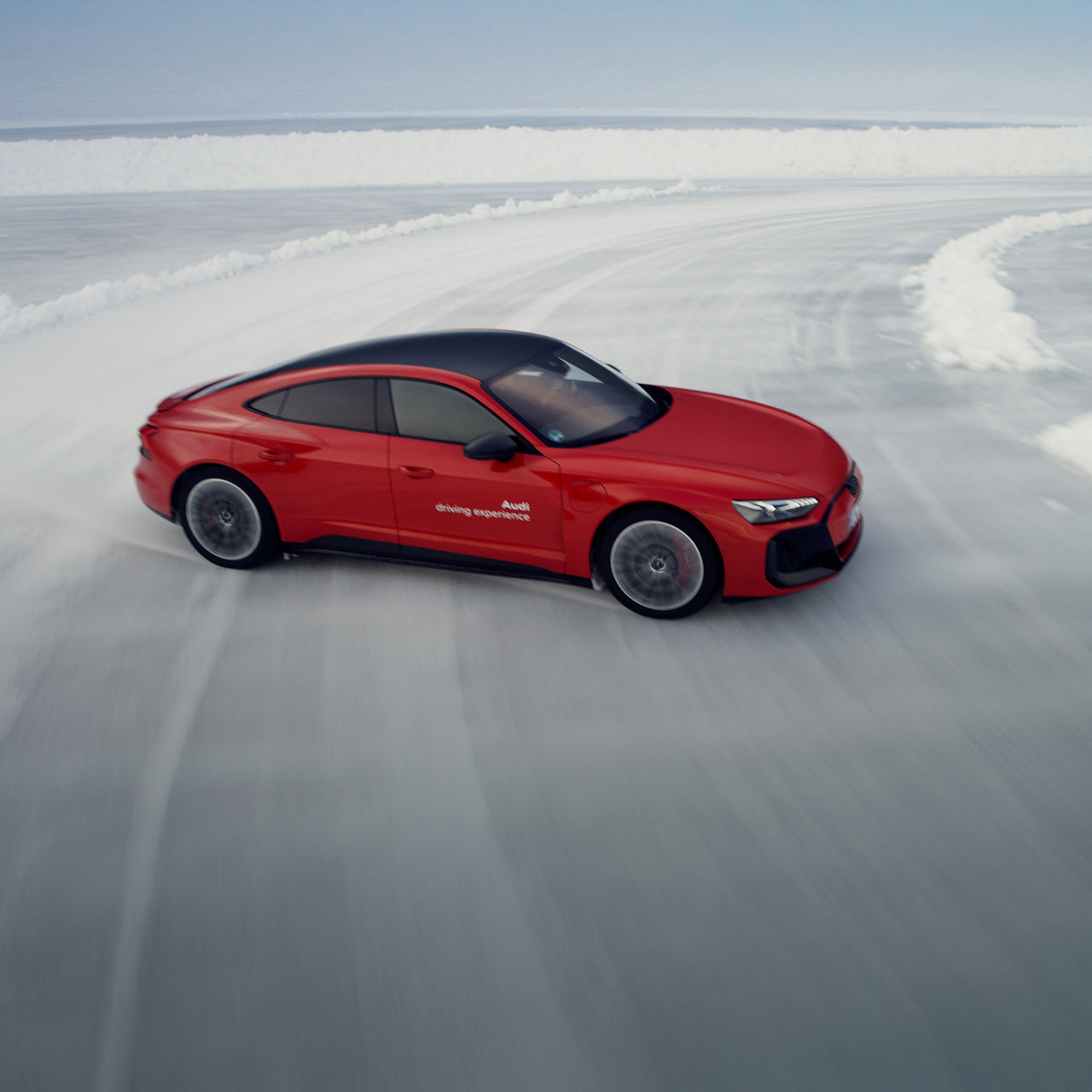  Ein roter Audi fährt auf einer vereisten Teststrecke und driftet durch eine scharfe Kurve, umgeben von Schnee.