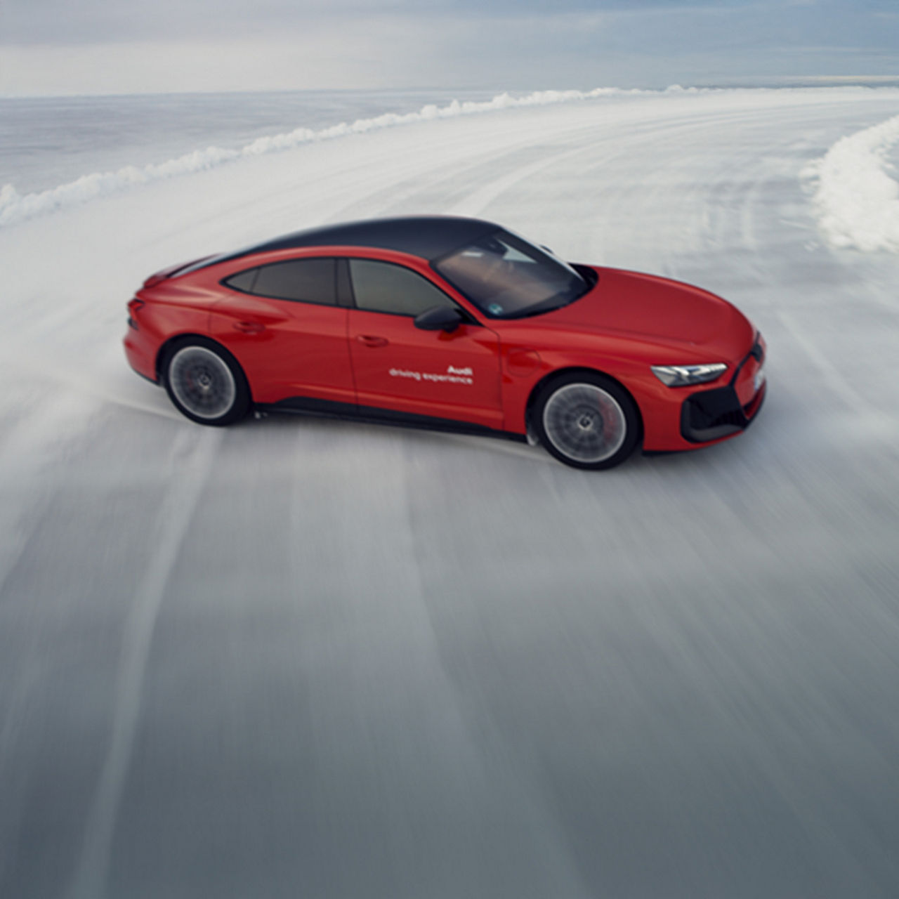  Ein roter Audi fährt auf einer vereisten Teststrecke und driftet durch eine scharfe Kurve, umgeben von Schnee.