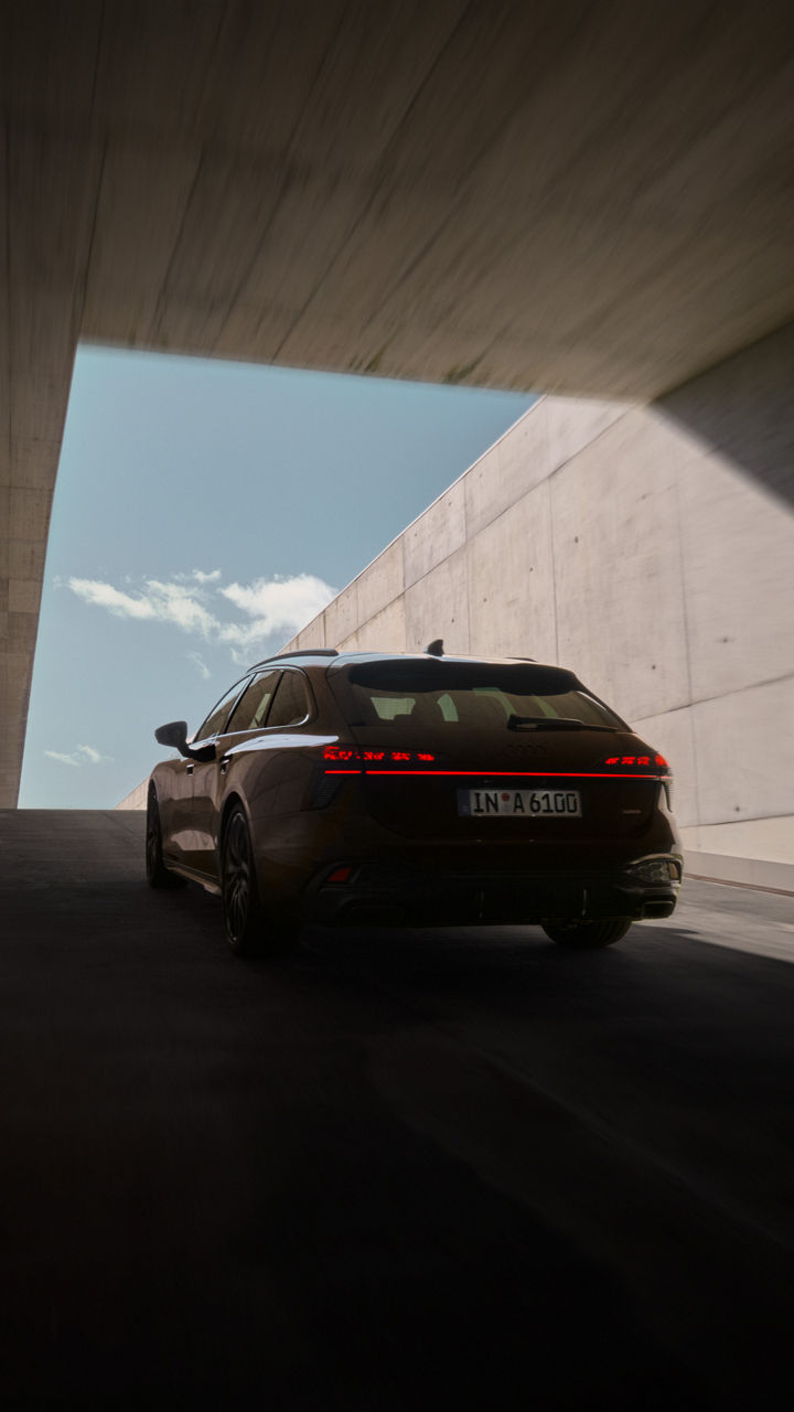 Audi A6 Avant in dunklem Braun fährt aus einem Tunnel heraus. Die Perspektive zeigt die Heckansicht des Fahrzeugs.