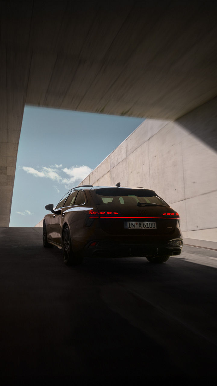 Audi A6 Avant in dunklem Braun fährt aus einem Tunnel heraus. Die Perspektive zeigt die Heckansicht des Fahrzeugs.