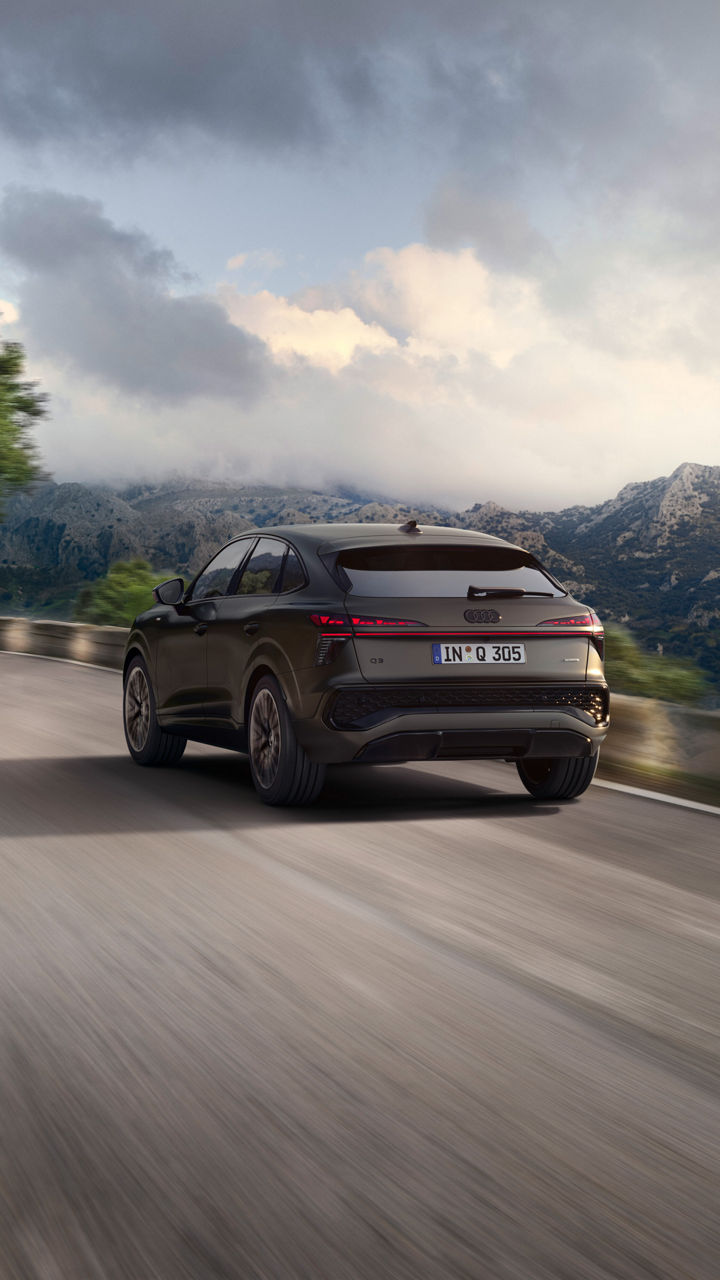 Ein Audi Q3 Sportback in dunklem Grau auf einer Bergstraße aus der Heckansicht fotografiert
