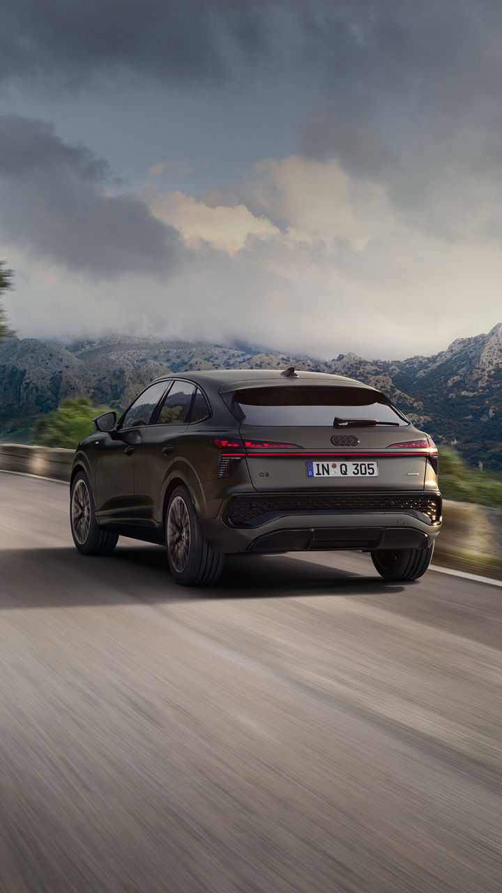 Ein Audi Q3 Sportback in dunklem Grau auf einer Bergstraße aus der Heckansicht fotografiert