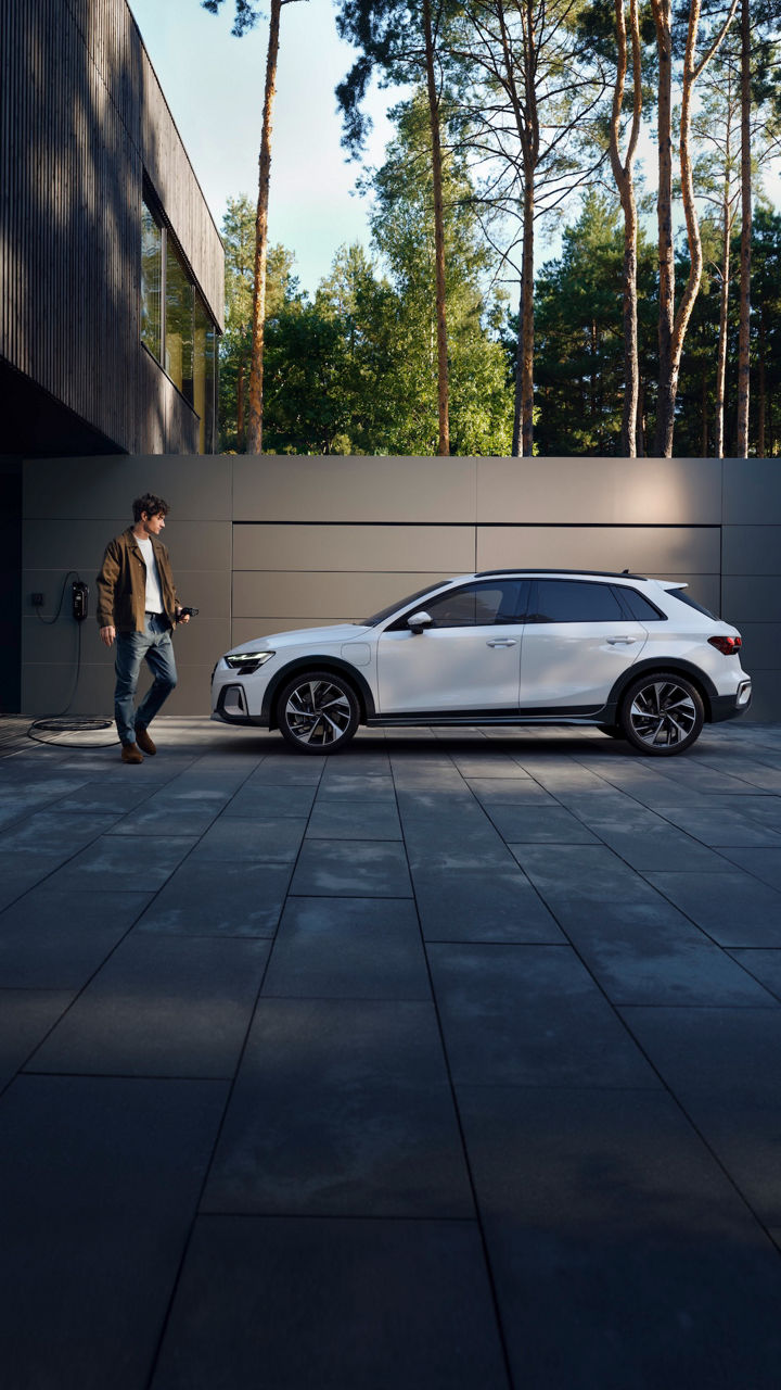 Audi A3 allstreet TFSI e parcheggiata, un uomo si avvicina per collegare il cavo di ricarica elettrica