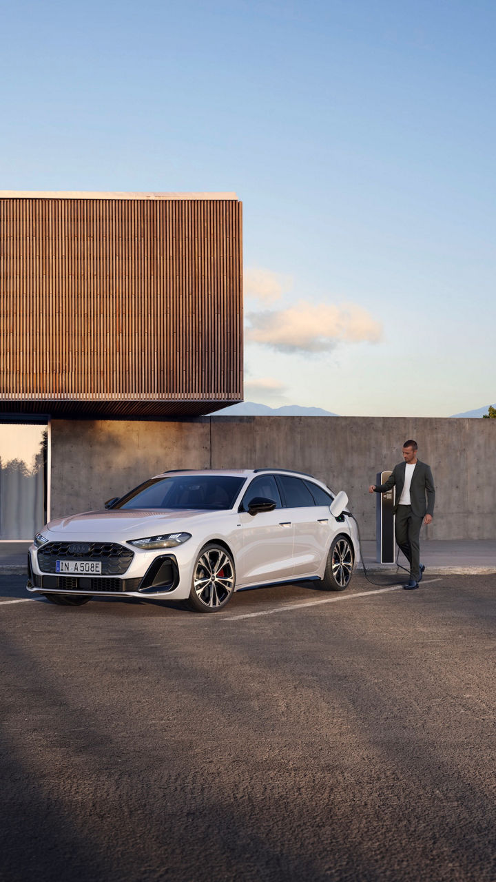 Audi A5 Avant e-hybrid parcheggiata e in ricarica elettrica, un uomo si avvicina per staccare la presa di collegamento