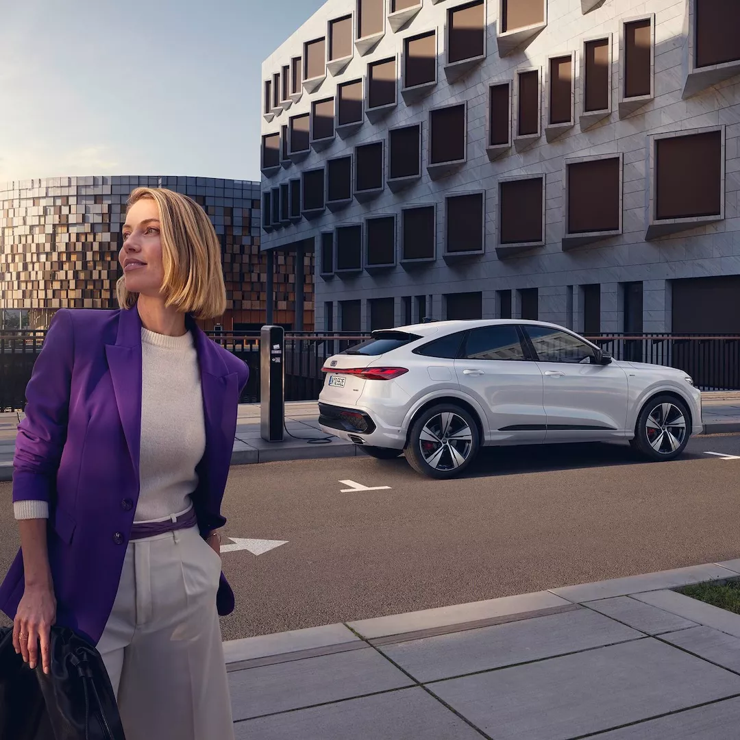 Una donna e sullo sfondo Audi Q5 Sportback e-hybrid parcheggiata e collegata a una colonnina di ricarica
