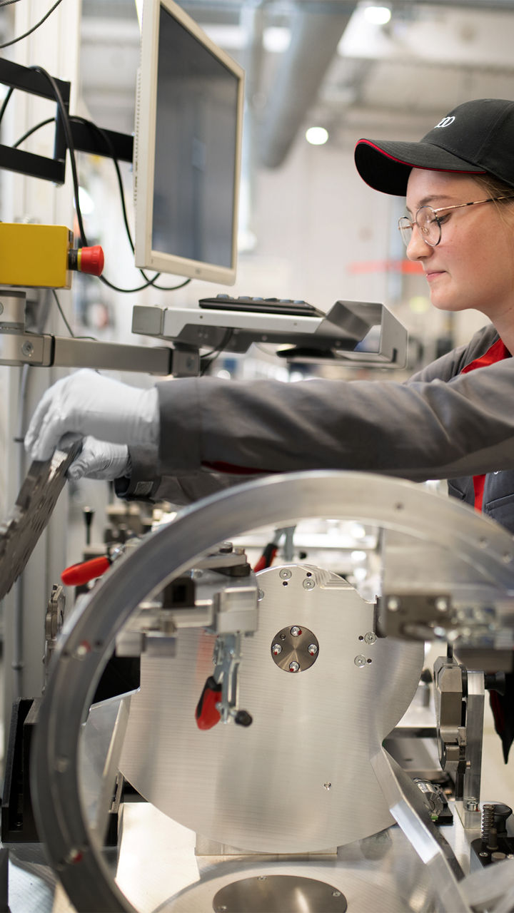 Man stands in a workshop with two parts of an Audi in his hand and looks into the camera