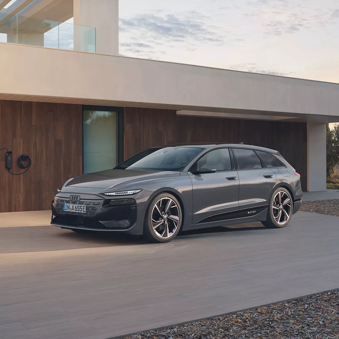 Grauer Audi A6 Avant e-tron parkt vor einem modernen Wohnhaus.