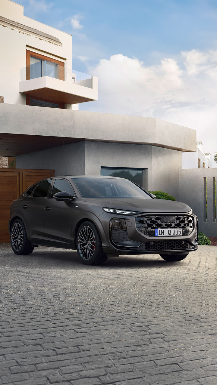 Audi Q3 Sportback gris foncé stationnée devant une maison moderne avec portail en bois