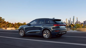 Un Audi Q6 e-tron SUV gris foncé roule sur une route avec une ligne d'horizon en arrière-plan.