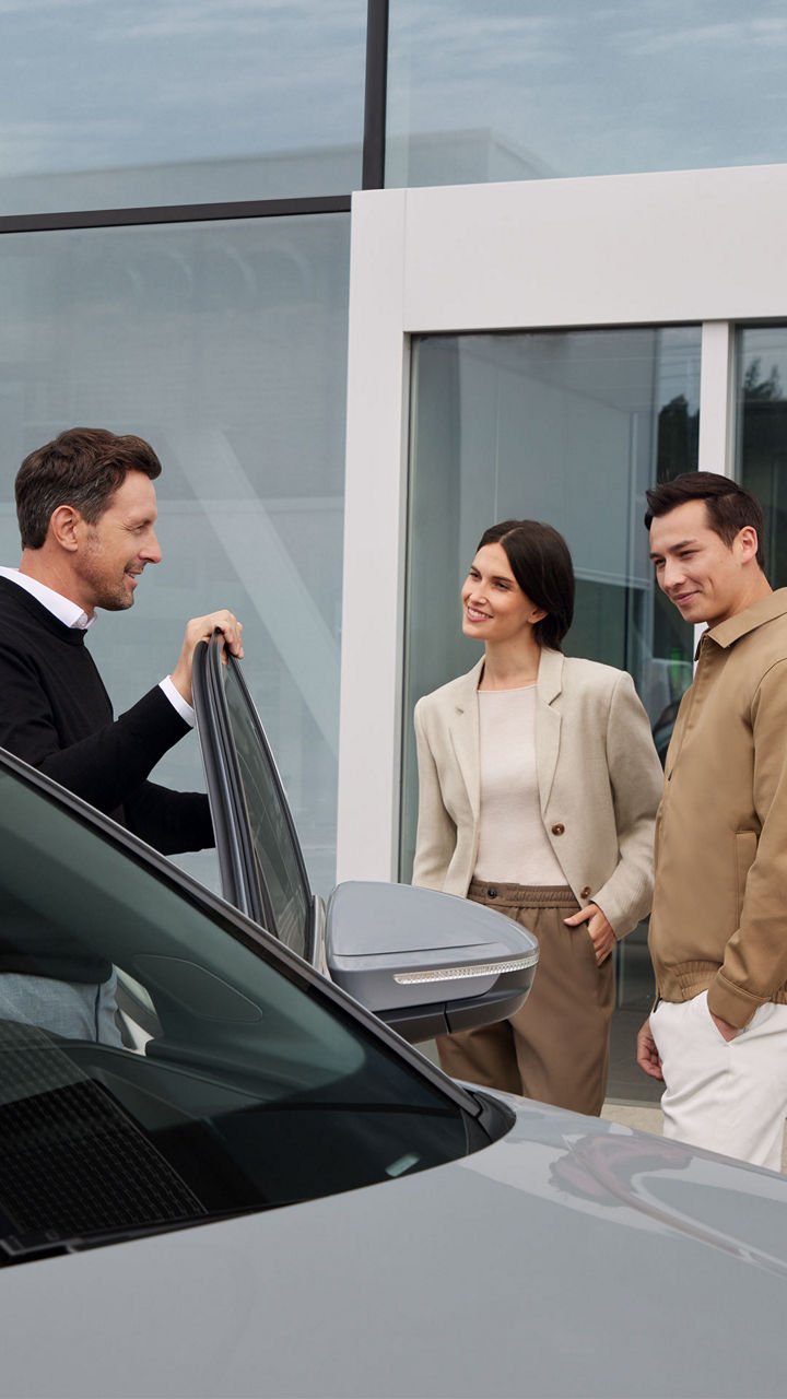 Un employé d'Audi se tient dans la portière du conducteur d'une voiture et discute avec un couple de clients.