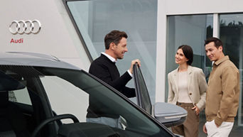 Audi Mitarbeiter steht in der Fahrertür eines Autos und unterhält sich mit einem Kundenpaar.