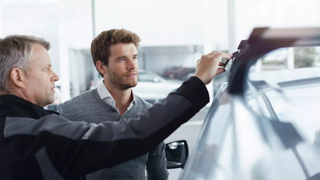 Närbild på händer som sätter fast en röd kanot på taket av en blå Audi Q3