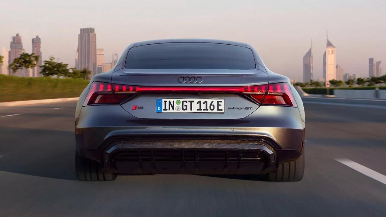 The rear of an R8 e-tron GT electric vehicle on a road driving towards the cityscape in the distance