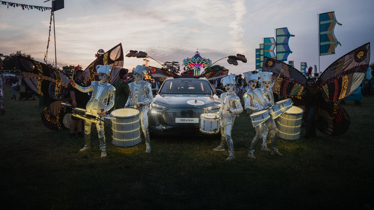 Several people dressed with customs, holding drums and dancing around an Audi car