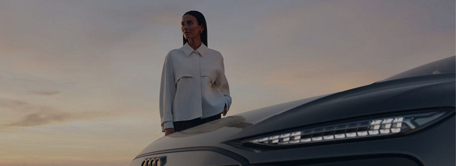 Person in a white shirt leaning on an Audi car at dusk.