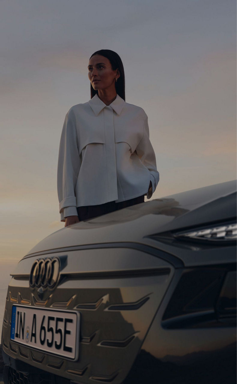 Person in a white shirt leaning on an Audi car at dusk.