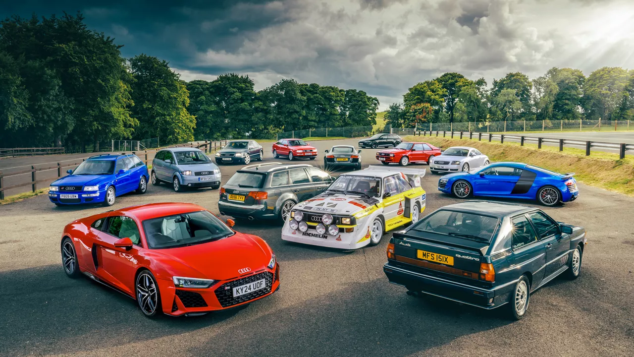 Two Audi racing cars among other racing cars on a track with a crowd in the background and advertising banners above