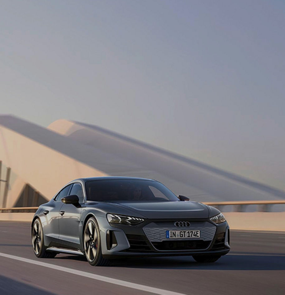 A grey Audi drives along a modern road, showcasing its stylish design against a minimalist architecture backdrop.