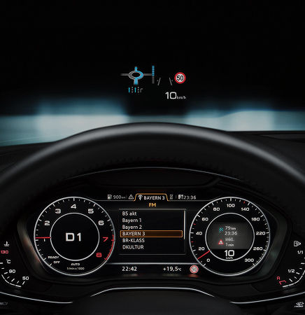 A close-up of a car's digital dashboard displaying radio stations, speed limits, and navigation information.