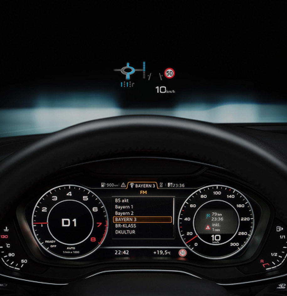 A close-up of a car's digital dashboard displaying radio stations, speed limits, and navigation information.