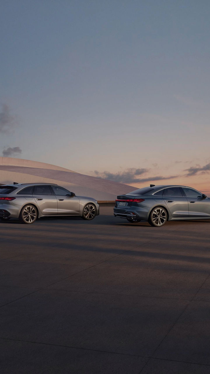 Two Audi cars parked under a pastel sunset sky, showcasing modern design against a minimalist architectural backdrop.