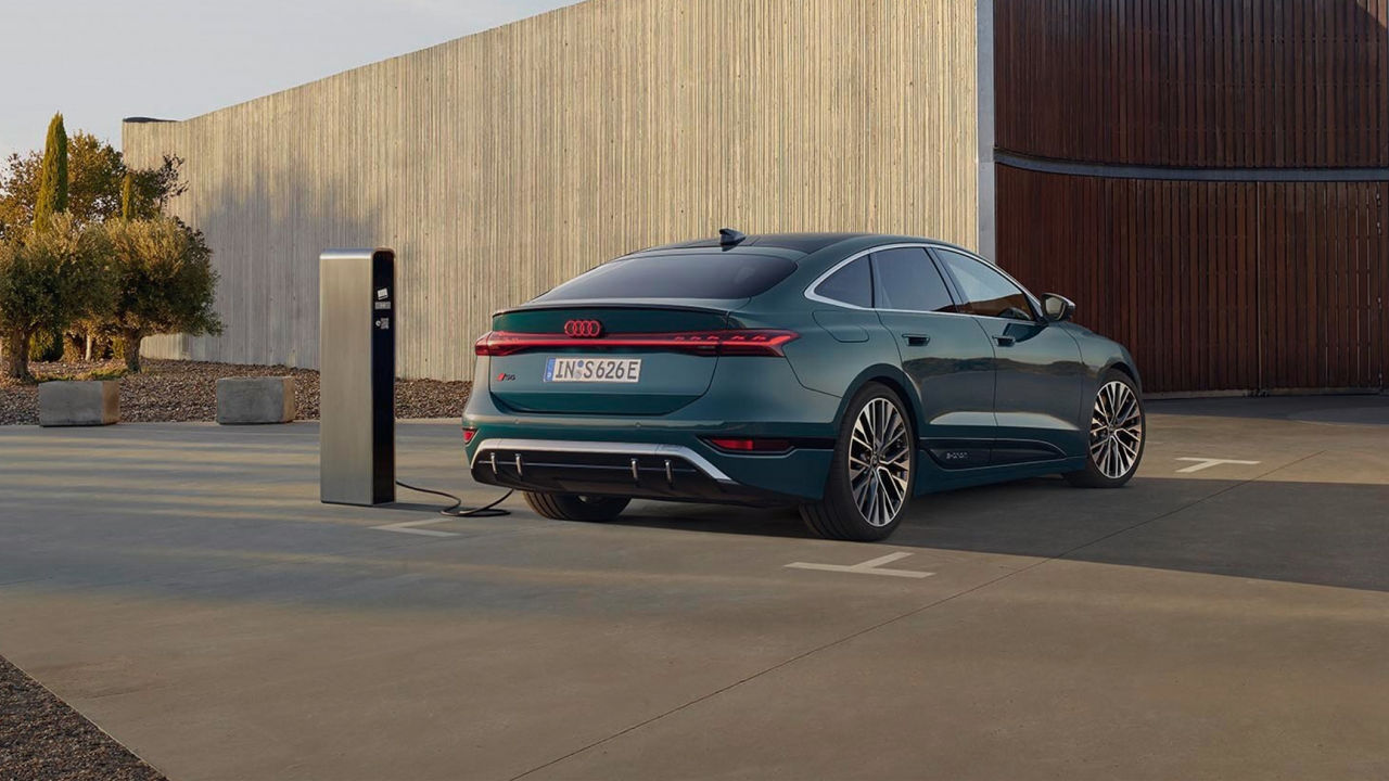 A man in a suit walking away from a parked Audi electric vehicle on charge at a charge station