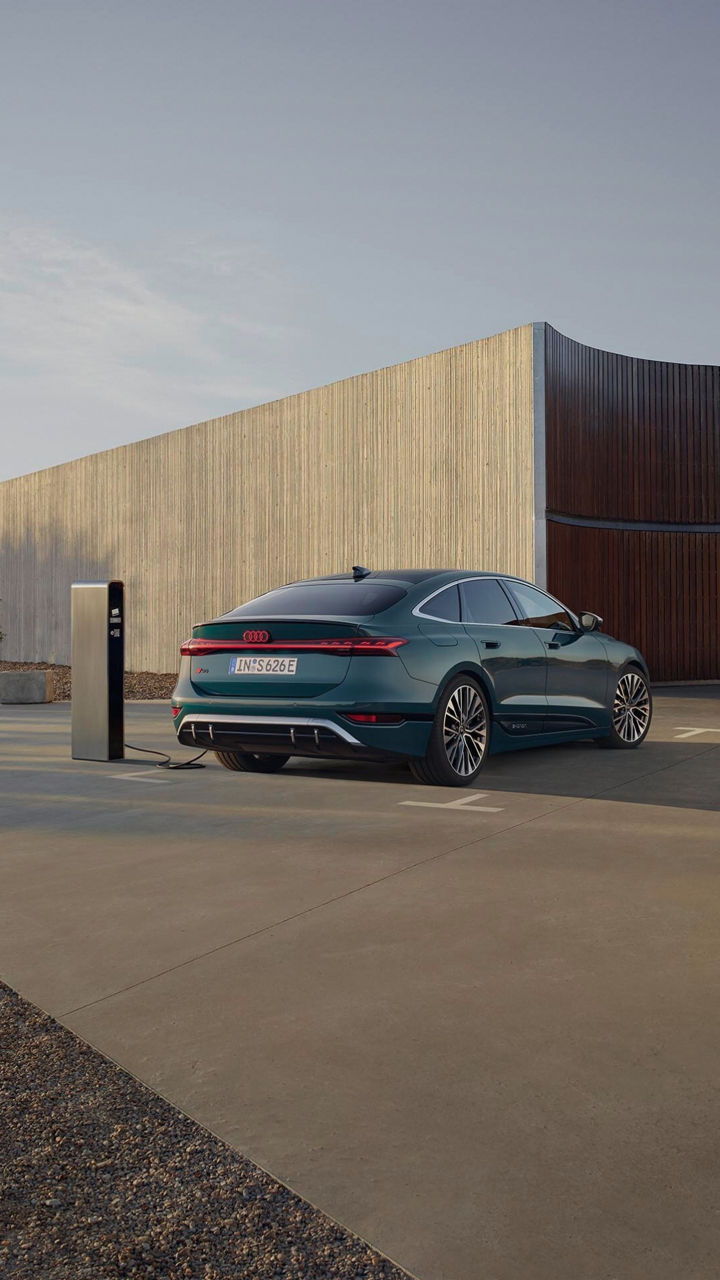 A man in a suit walking away from a parked Audi electric vehicle on charge at a charge station