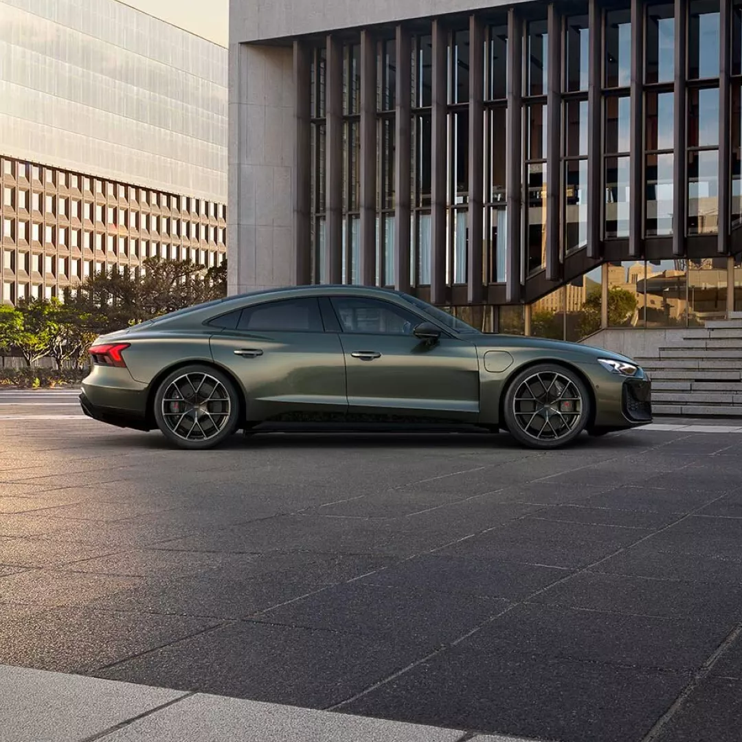 A sleek green sports sedan parked on a city street, with modern buildings and a textured pavement visible in the background.