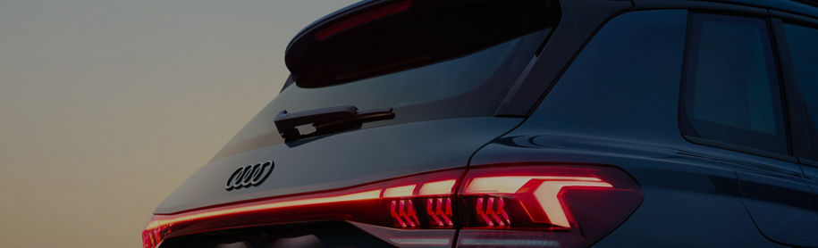 Close-up of an Audi vehicle's rear end showcasing sleek taillights and the iconic logo against a soft twilight background.