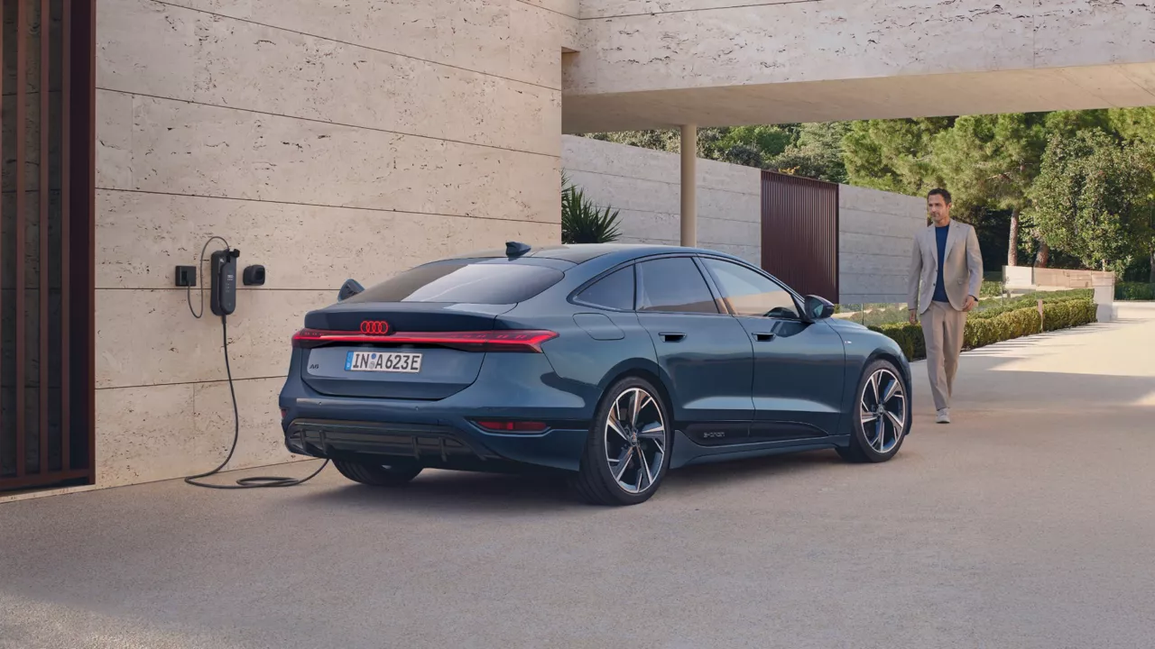 Blue Audi electric vehicle rear view while connected to a charger on a wall and man walking towards it