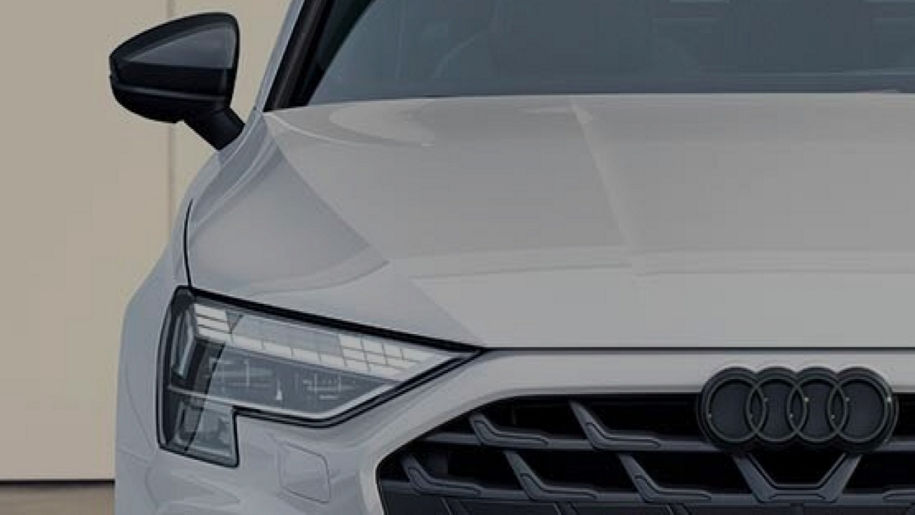 Front view of a white Audi, showcasing its modern grille and sharp headlights, with a stylish side mirror partially in view.