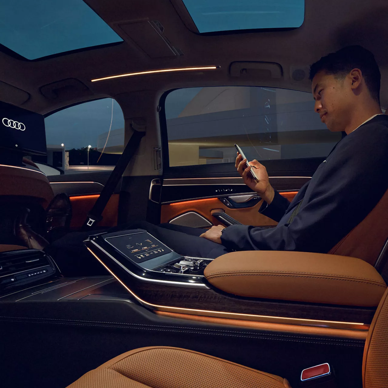 Man sitting inside an Audi vehicle, on the passenger seat, browsing his mobile phone