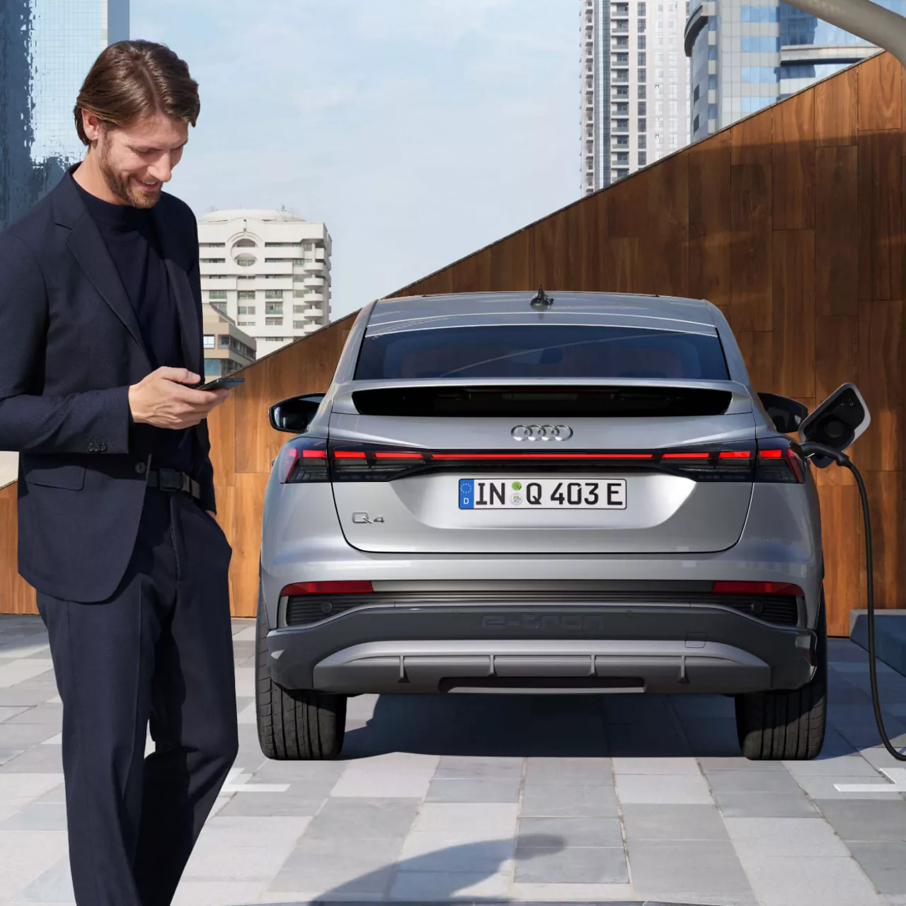 Man, looking at his phone, walking past an Audi Q4 e-tron being charged outdoors