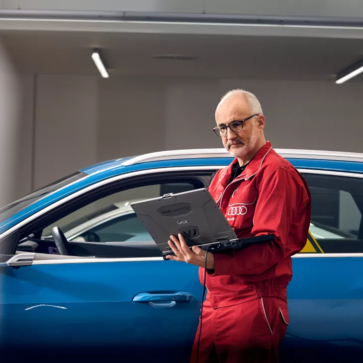 Audi technician holding a laptop, in front of an Audi vehicle