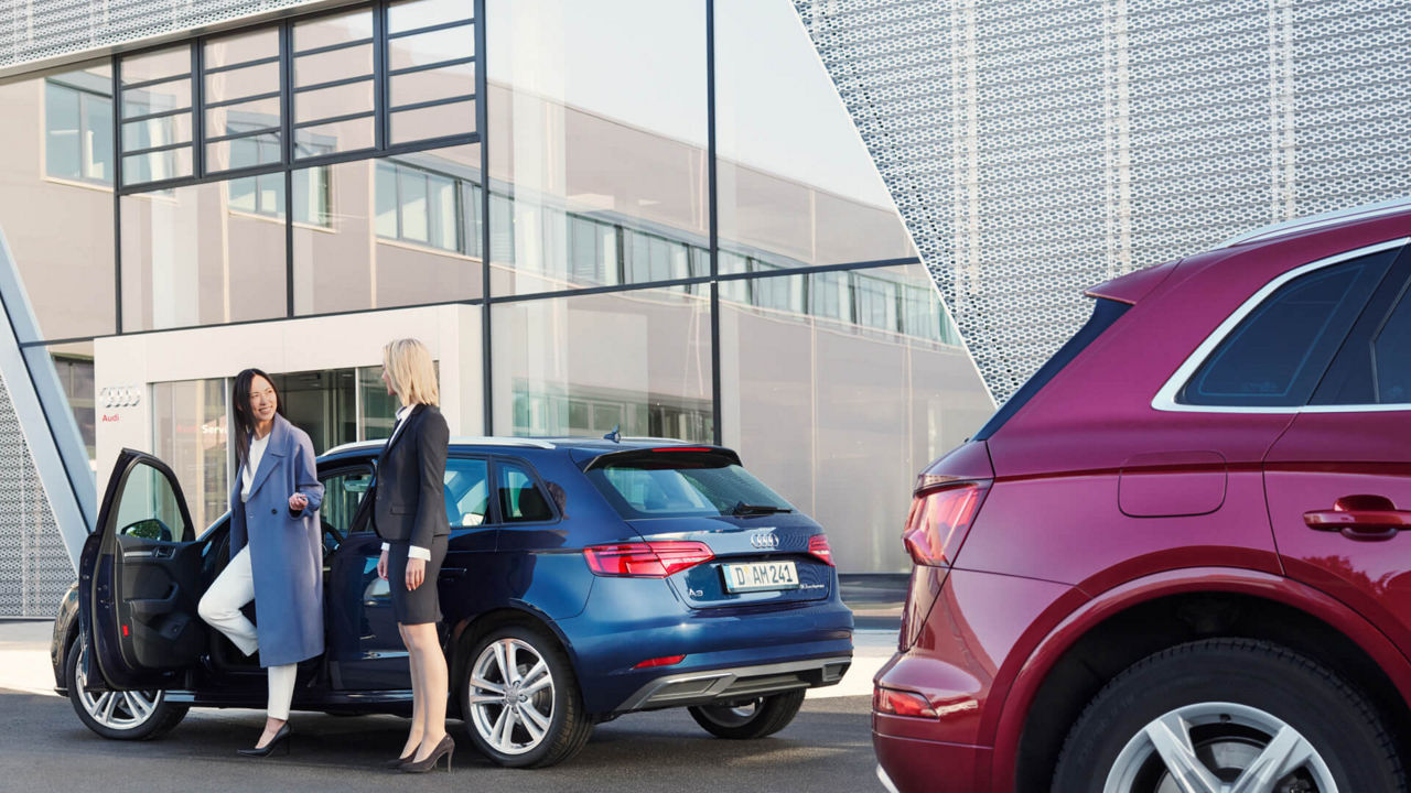 Two women chatting, standing by a dark blue Audi vehicle