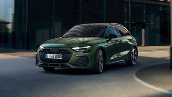 A green Audi A3 Sportback drives dynamically on a modern city street, showcasing its stylish design and sporty features.