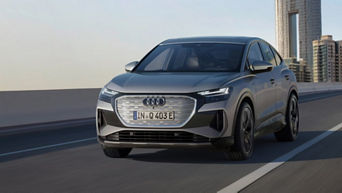 A grey Audi Q4 Sportback e-tron driving on a modern highway with a city skyline in the background against a clear sky.