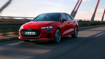 A red Audi A3 Saloon driving on a bridge, showcasing its dynamic design against a backdrop of a clear sky.