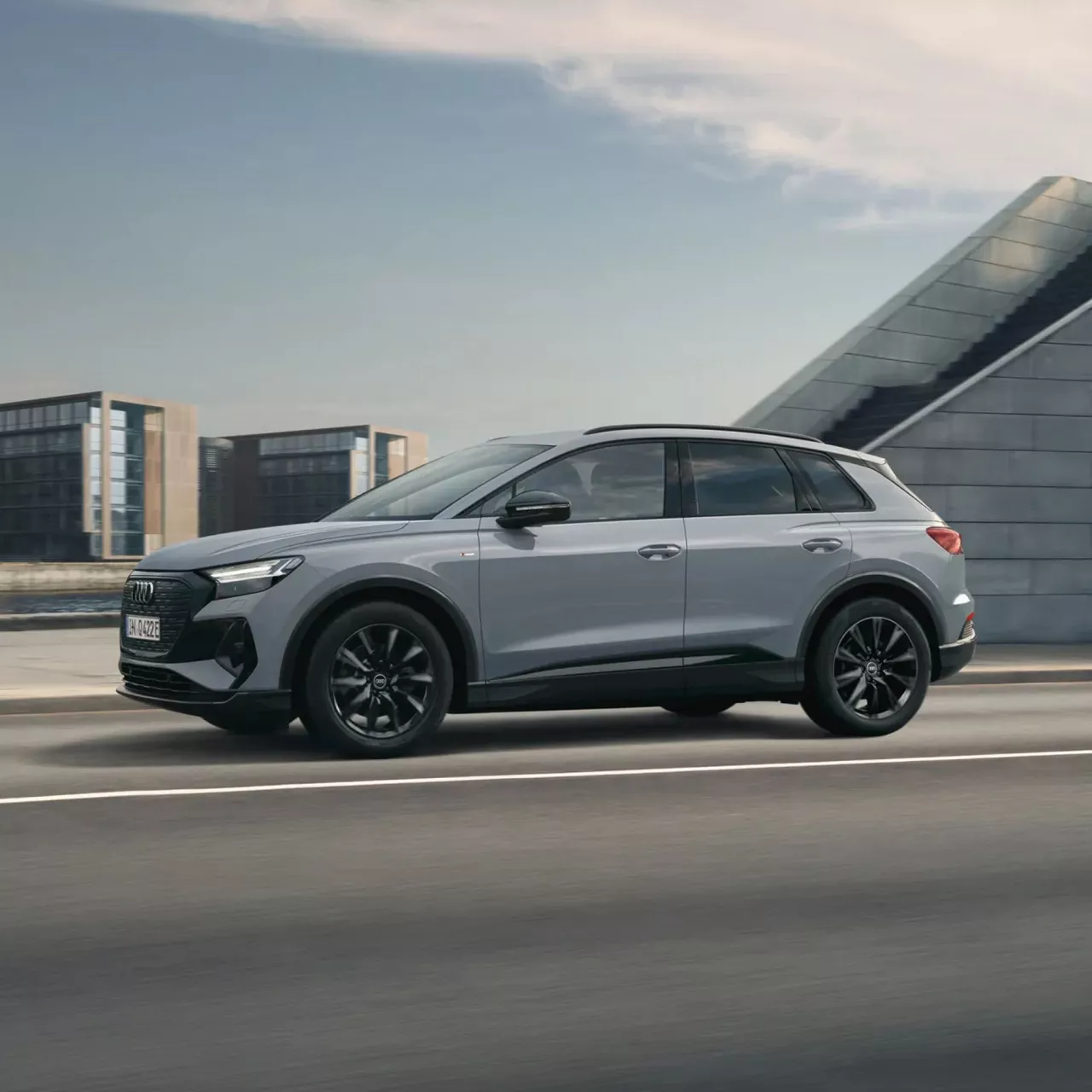 Silver SUV Audi Q4 e-tron driving on road with modern buildings in the background.