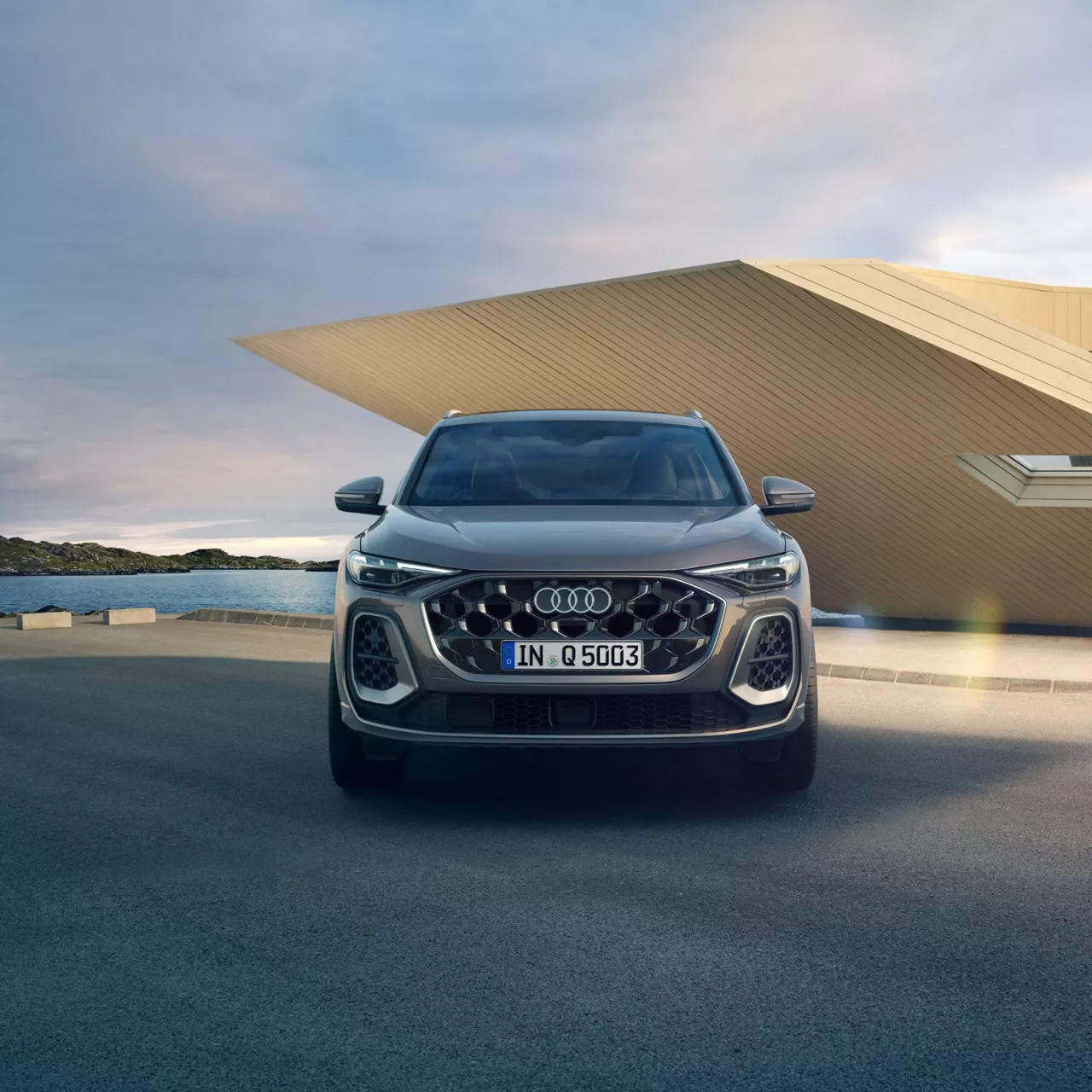 A silver Audi Q5 SUV parked in front of a modern building with a coastal backdrop.