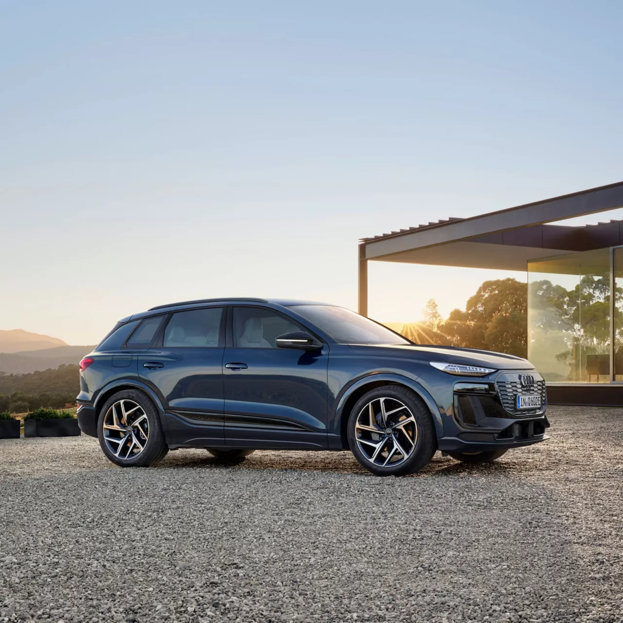 Blue Audi Q6 SUV e-tron parked outside a modern house at dusk.