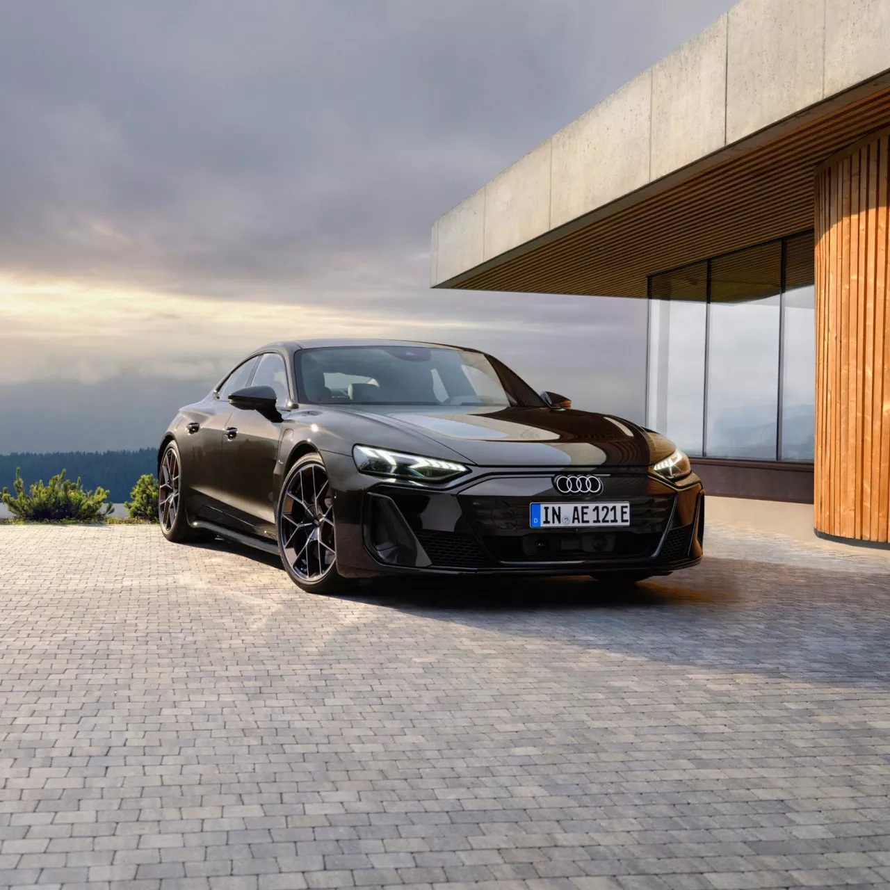 A black Audi S e-tron GT car parked in front of a modern house with an overcast sky.