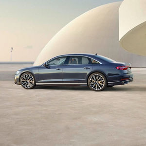 A blue luxury sedan parked on a minimalist surface with a modern curved structure in the background during golden hour.