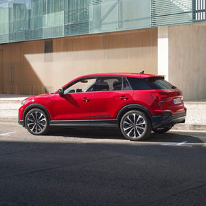 A red Audi Q2 parked on a city street, showcasing modern design elements and reflections from a contemporary building nearby.
